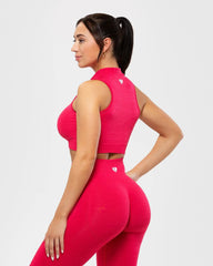 المنظر الخلفي لامرأة ترتدي حمالة صدر رياضية وردية اللون وسروالًا ضيقًا، مع تانك قصير بدون خياطة بنصف سحاب للنساء من تصميم Viva Magenta.