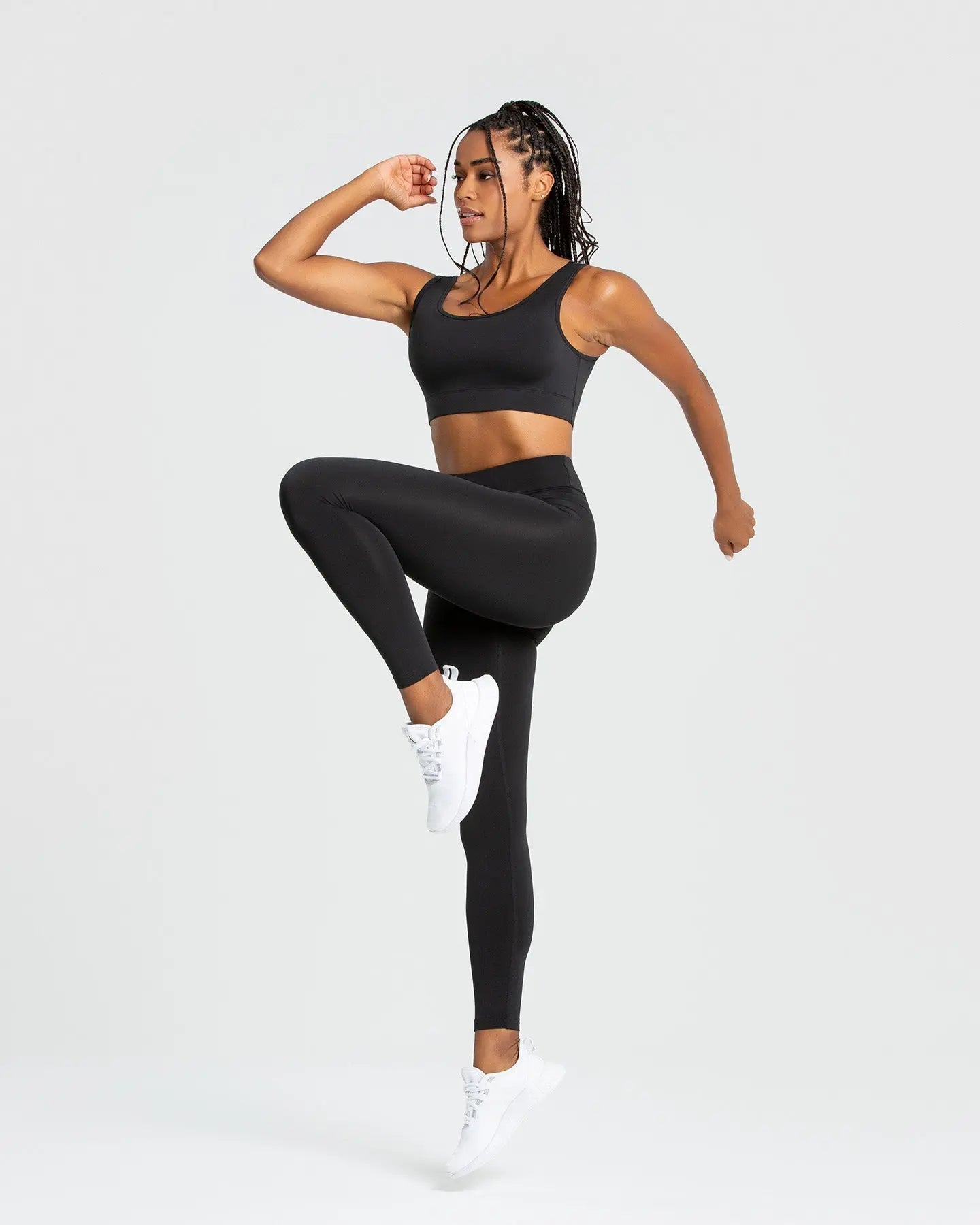 امرأة سوداء ترتدي أفضل السراويل الضيقة الأساسية للنساء | حمالة صدر رياضية سوداء وسراويل ضيقة على خلفية بيضاء سادة، تعرض أقصى درجات الراحة والاستخدامات المتعددة لهذه السراويل الضيقة الأساسية للسيدات | أسود.
