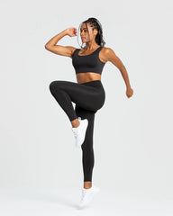 امرأة سوداء ترتدي أفضل السراويل الضيقة الأساسية للنساء | حمالة صدر رياضية سوداء وسراويل ضيقة على خلفية بيضاء سادة، تعرض أقصى درجات الراحة والاستخدامات المتعددة لهذه السراويل الضيقة الأساسية للسيدات | أسود.