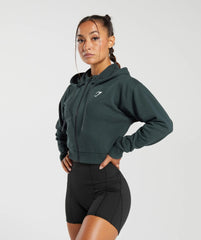 امرأة ترتدي سترة GS Power Crop Zip باللون الأخضر المريح مع جيوب جانبية وسروال قصير أسود.